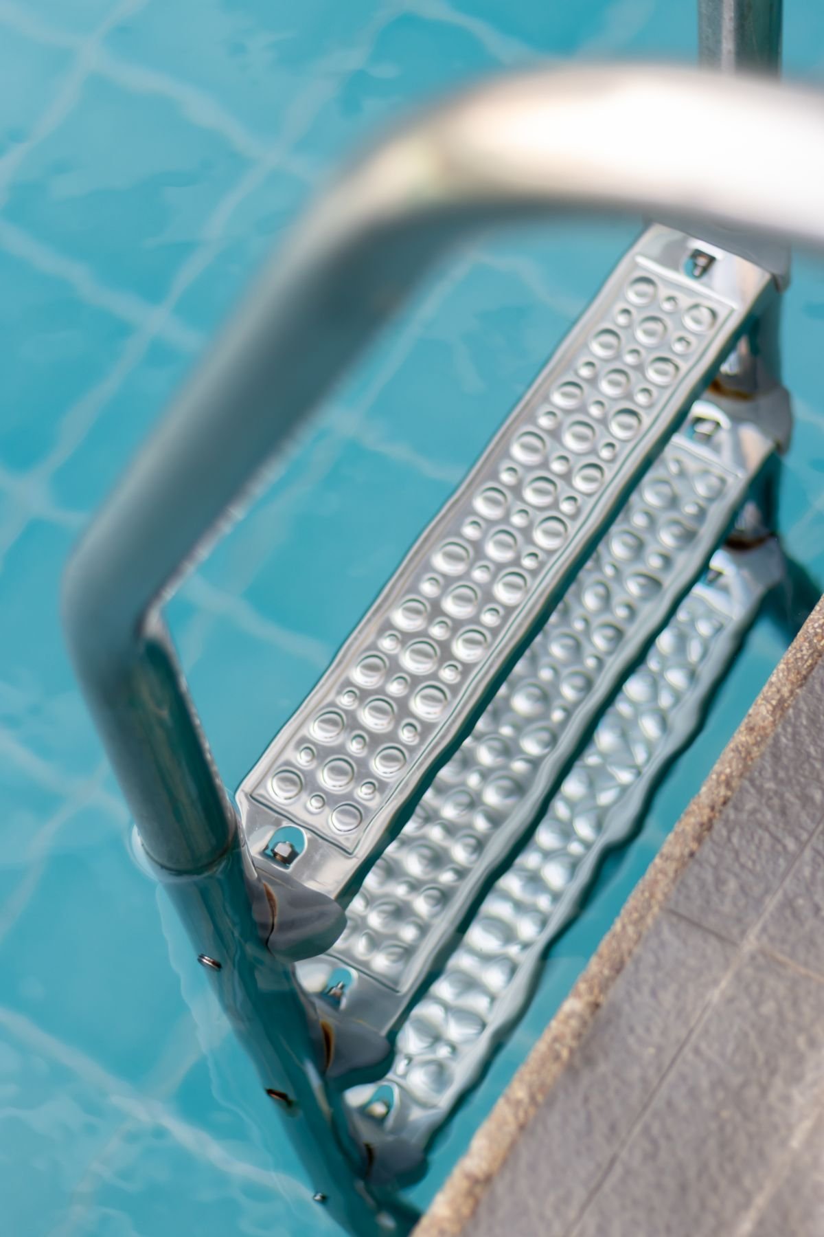 Stainless steel ladder steps in a clear blue swimming pool